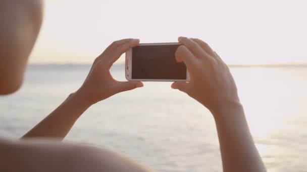 Plajda gün batımını cep telefonuyla çeken bir turist. — Stok video