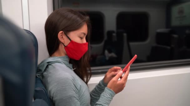 Femme portant un masque facial dans les transports publics pendant la pandémie de coronavirus Covid-19. Concept de transport ferroviaire de banlieue. Passager femme multiraciale utilisant un téléphone intelligent avec couverture du visage sur le trajet. — Video