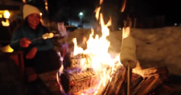 Vacaciones de invierno estación de esquí mujer tostado malvaviscos en barbacoa firepit. Afterski actividad divertida con amigos. Pareja de malvavisco a la parrilla en palo en el fuego. — Vídeos de Stock