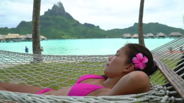 Podróże wakacje na plaży Luksusowy ośrodek wypoczynkowy kobieta relaksująca się leżąc w hamaku przy nadwodnych bungalowach hotelu na Bora Bora, Tahiti, Polinezja Francuska. Szczęśliwego wakacyjnego wyjazdu. — Wideo stockowe