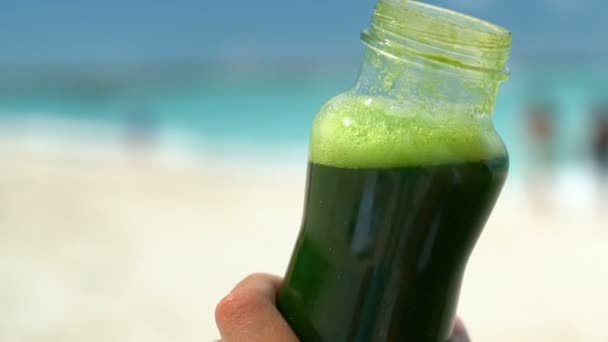 Ruční držení zeleninové smoothie láhev na pláži - zdravé dietní detox džus — Stock video