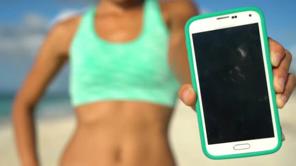Femme sportive montrant un téléphone intelligent sur la plage Gros plan de l'écran de téléphone intelligent — Video