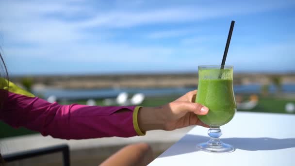 Nő kezében zöld smoothie üveg ivás spenótlé kívül kávézó asztal — Stock videók