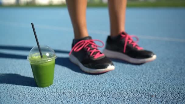 Sapatos de fitness e copo de suco de smoothie verde na pista de corrida — Vídeo de Stock