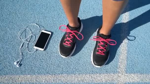 Running παπούτσια γυναίκα κρατώντας smartphone και ακουστικά για μουσικά κίνητρα — Αρχείο Βίντεο
