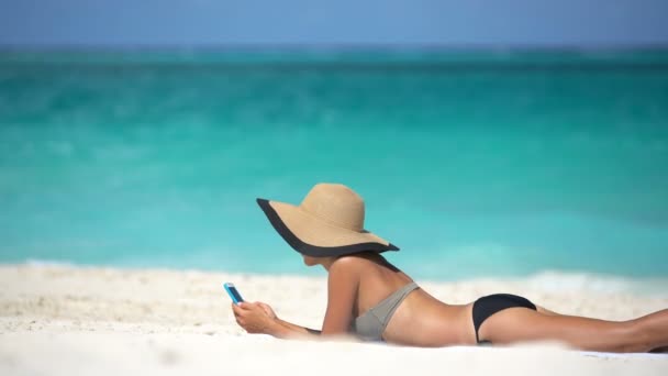Žena pomocí telefonní aplikace na pláži na letní dovolenou opalování — Stock video