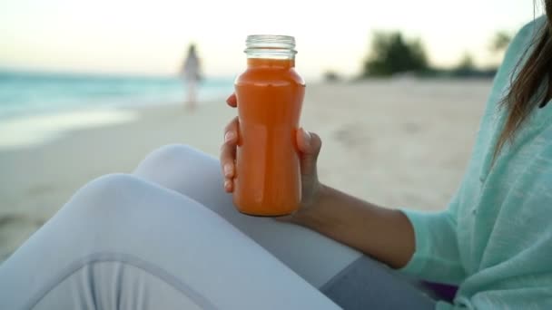 Cold pressed juice - κοντινό πλάνο της γυναίκας πίνοντας χυμό καρότου στην παραλία — Αρχείο Βίντεο