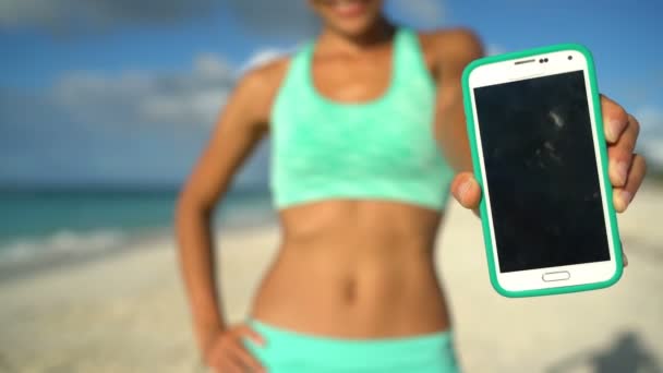 Mujer Deportiva Mostrando teléfono inteligente en la playa - Primer plano de la pantalla del teléfono inteligente — Vídeos de Stock