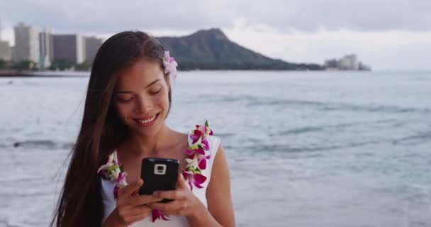 Улыбающаяся молодая женщина фотографируется со смартфоном на пляже Уэйки — стоковое видео