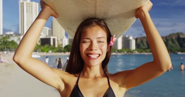 Uśmiechnięta młoda kobieta niosąca deskę surfingową na głowie na plaży Waikiki — Wideo stockowe