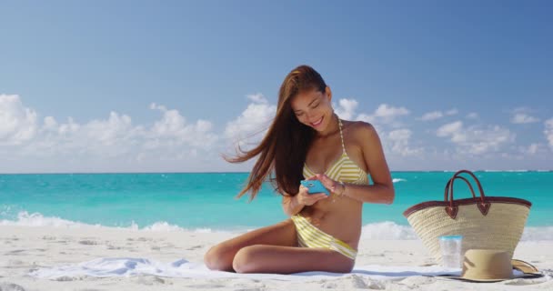 Mujer usando aplicación de teléfono inteligente en la playa bikini chica mirando teléfono celular relajante — Vídeo de stock