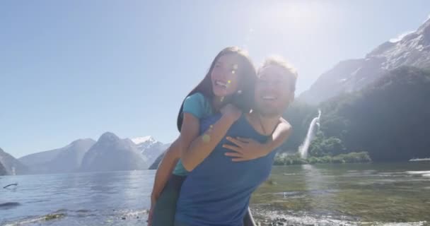 Couple piggybacking having fun outdoors in nature in Milford Sound New Zealand — Stock Video