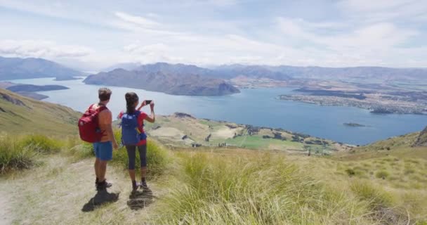 Pareja de senderismo tomando fotos con teléfono en la cima de la montaña Roys Peak, Nueva Zelanda — Vídeo de stock