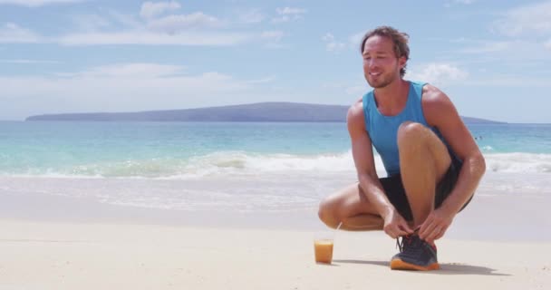 Läufer schnürt Laufschuhe und trinkt kaltgepressten Karottensaft am Strand — Stockvideo