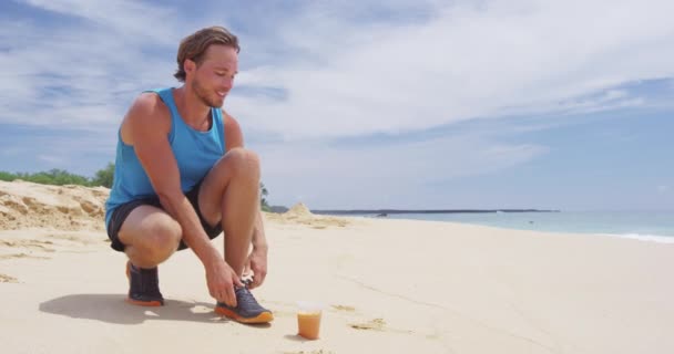 Biegacze wiążą sznurowadła na butach do biegania pijąc zimny sok marchewkowy na plaży — Wideo stockowe