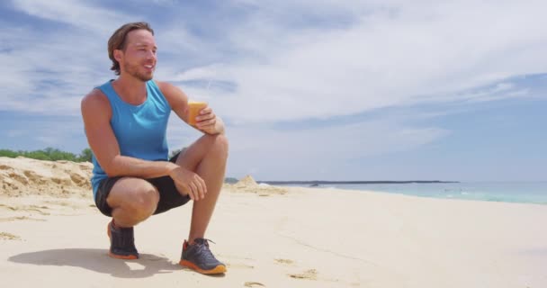 Man die koud geperst wortelsap drinkt op het strand na het rennen — Stockvideo
