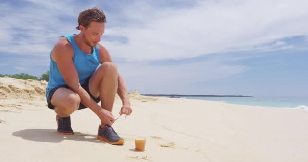 Corredor atar cordones en zapatillas de correr beber jugo de zanahoria prensado en frío en la playa — Vídeo de stock