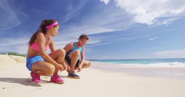 Koşan bir çift koşu ayakkabılarını bağlıyor plajda koşuya hazırlanıyor. — Stok video