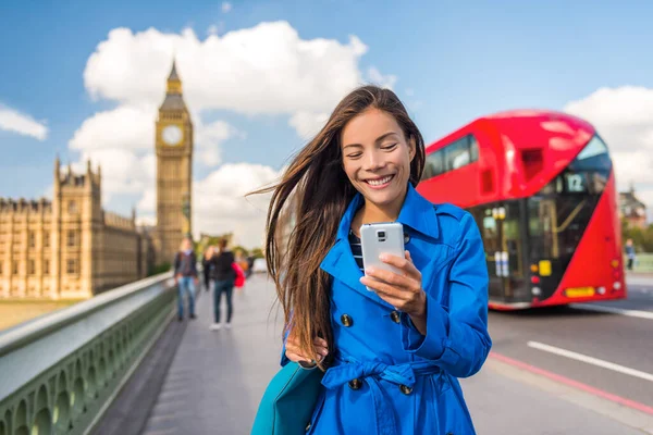 Londralı telefon işçisi ödemeyi ya da online alışverişi için akıllı telefon uygulaması üzerinden mesaj atıyor. Şehirdeki Asyalı kız Big Ben ve kırmızı otobüs geçmişinde mutlu mesut yürüyor. — Stok fotoğraf