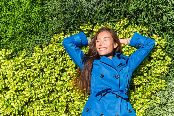 Natura relax felice primavera cappotto donna sdraiata su sfondo verde erba texture. Asiatico sorridente ragazza in giacca stile moda — Foto Stock