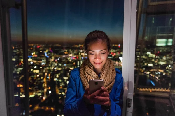 London urban people city lifestyle woman using phone app texting sms on social media. Young Asian girl holding cellphone at night on skyline background — Stock Photo, Image