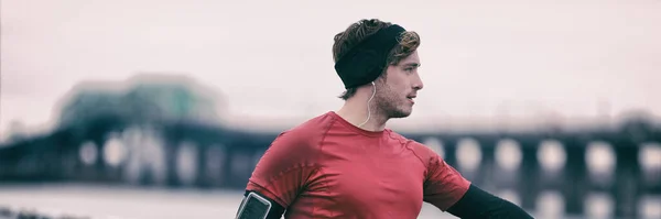 Inverno corridore uomo in aria fredda all'aperto formazione cardio. Maschio corridore che si estende dopo aver corso in autunno indossando abbigliamento da corsa sport caldo. Bellissimo modello di sport di fitness maschile all'aperto. Panoramica — Foto Stock