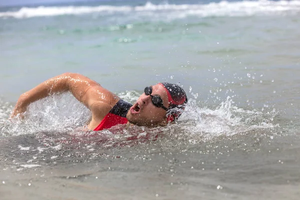 Profesjonalny triatlonista pływający czołga się po oceanie. mężczyzna triathlon pływak noszenie czapki, gogle i czerwony triathlon tri garnitur szkolenia dla Żelazny oddychanie z wody — Zdjęcie stockowe