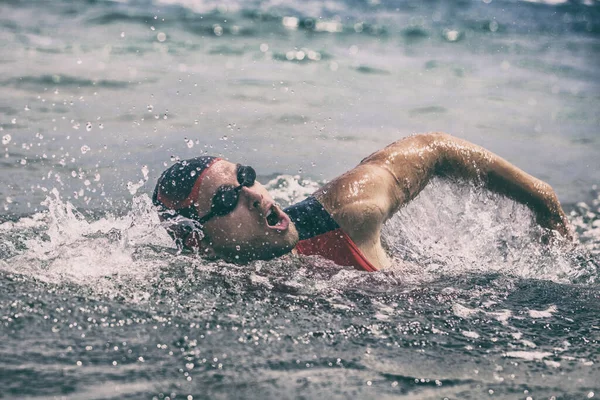 Triathlonrennen Schwimmer Schwimmen Freistil kriechen im Ozean. Triathlonprofi mit Schirmmütze, Brille und rotem Triathlonanzug trainiert Ironman beim Atmen aus dem Wasser — Stockfoto