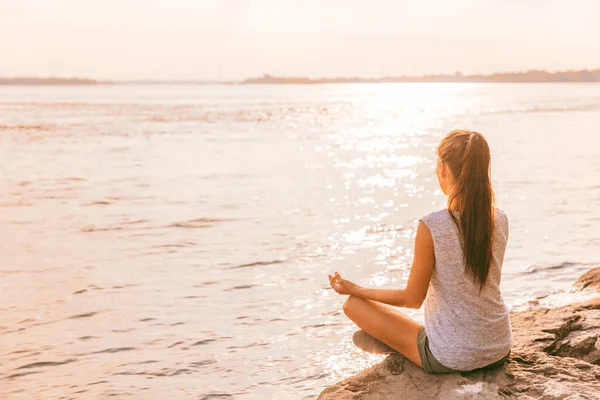 Здоровая женщина йоги медитирует на рассвете у озера. Пляжная медиация велнес-девушка наслаждается летним солнцем. — стоковое фото