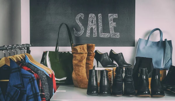 Compra de zapatos venta de zapatos y botas de invierno en los estantes de la tienda. Cartel de venta en fondo con abrigos de otoño y botines de cuero para mujer. — Foto de Stock