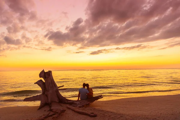 Par på stranden vid solnedgången silhuetter - sommar resor semester i Karibien destination. Romantisk strand par smekmånad älskare njuter av att titta på solnedgången sitter på trädstam vid havet — Stockfoto