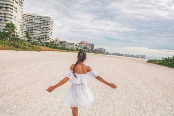 Bonne femme de plage en robe de soleil blanche dansant insouciant pendant les vacances d'été - style de vie de vacances. Fille libre joyeux avec les bras ouverts sur voyage romantique lune de miel avec robe blanche sans bretelles oeillet — Photo