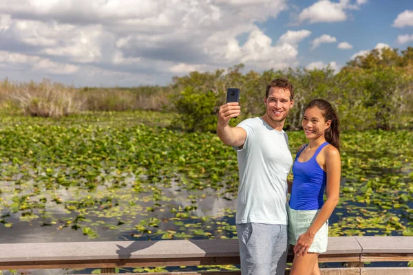 Florida travel tourists couple taking selfie photo at Everglades National park walking in wetlands Anhinga trail walkway boardwalk summer tourism lifestyle young people — Stock Photo, Image