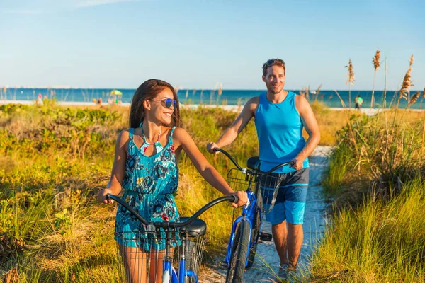 Summer people lifestyle happy couple biking on beach relaxing outdoors activity at sunset. Young woman and man riding leisure bicycles on USA Florida holidays getaway — Stock Photo, Image