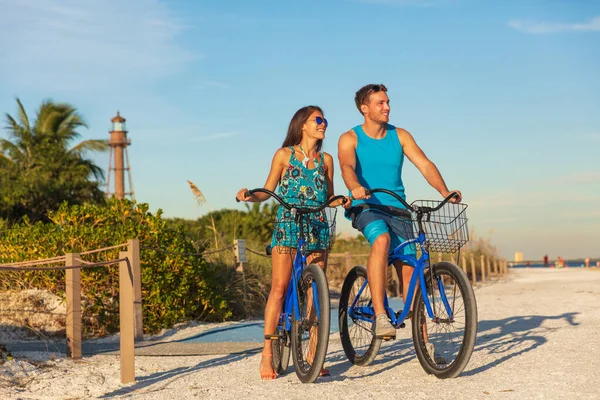 Florida sahilinde tatil yapan çiftler spor bisikletleri kiralayıp deniz fenerinin yanındaki Sanibel Adası 'nda günbatımını izlemekten mutluluk duyuyorlar. Genç kadın ve erkek bisiklete biniyor. Yaz insanları yaşam tarzı — Stok fotoğraf