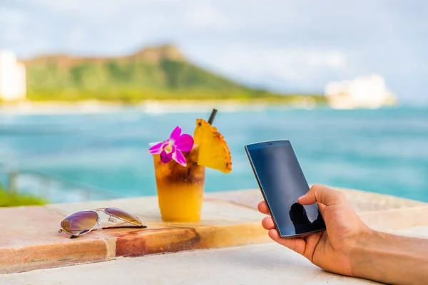 Phone app man texting taking mobile phone picture of Hawaii mai tai drink cocktail at Hawaii beach bar. Glass with flower, pineapple, sunglasses. Cellphone screen with diamond head, Honolulu vacation — Stock Photo, Image