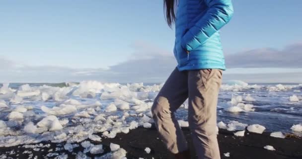 Женщина, идущая по алмазному пляжу со льдом из ледниковой лагуны Йокосарлон Исландия — стоковое видео