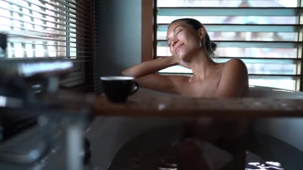 Bagno di lusso donna asiatica rilassante in acqua calda godendo la vista dalla finestra del bagno che giace nella vasca da bagno con vasca caddy bordo di legno. — Video Stock
