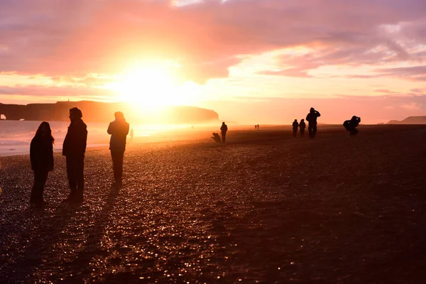 Τουρίστες σιλουέτα στην Ισλανδία στο ηλιοβασίλεμα με τα πόδια Reynisfjara μαύρη παραλία άμμο, Vik, Νότια ακτή της Ισλανδίας. Άτομα που επισκέπτονται τουριστικό προορισμό έλξης — Φωτογραφία Αρχείου