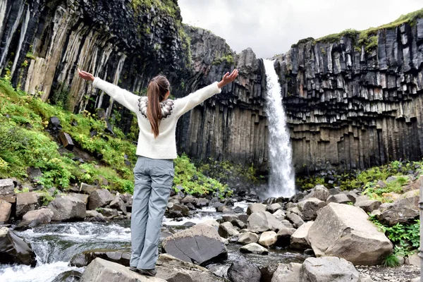 Islandia. Kobieta ciesząca się majestatycznym wodospadem Svartifoss. Kobieta odwiedza słynną atrakcję turystyczną Islandii. Spektakularny naturalny punkt orientacyjny na wakacjach w Skaftafell. Krajobraz przyrodniczy Islandii — Zdjęcie stockowe