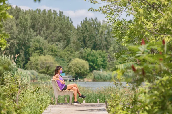 PALABRAS CLAVE COPIADA DE BANNER Máscara con mujer sentada relajada en el banco afuera en el parque natural de verano para la prevención del coronavirus. Proteger la cara que cubre el estilo de vida COVID-19. Banner panorámico —  Fotos de Stock