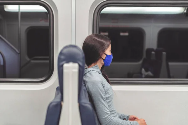 Tren yolculuğu sırasında pencereden dışarı bakan, toplu taşıma araçlarında maske takan bir kadın. Coronavirus pandemik yaşam tarzı. Yolcu banliyö yolcusu bez ağız örtüsü kullanıyor. — Stok fotoğraf