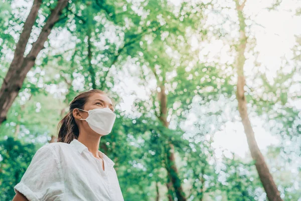 Mask wearing woman looking up to bright future in hope walking in forest. Sustainable fashion fabric in PPE, asian girl lifestyle breathing clean air — Stock Photo, Image