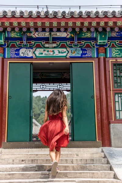 중국의 여름 여행인 고대 황제 사원에 있는 오래 된 나무로 된 전통적 인 중국 문을 걸어 다니는 고상 한 여자. 바람에 나부끼는 빨간 드레스를 입고 있는 멋진 소녀 — 스톡 사진