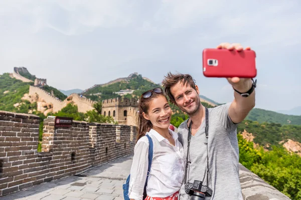 Glada par turister som tar selfie bild på Great Wall of Kina, topp världsomspännande turistmål. Unga multiracial människor som använder telefon fotografering app för foton — Stockfoto