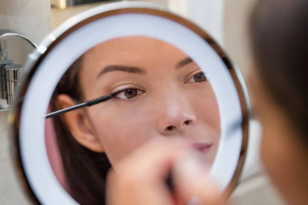 Mujer poniendo rímel en anillo de luz redonda espejo de maquillaje en casa rutina de baño por la mañana. Hermosa chica asiática preparándose para aplicar maquillaje de ojos con cepillo. Primer plano en el ojo en reflexión — Foto de Stock