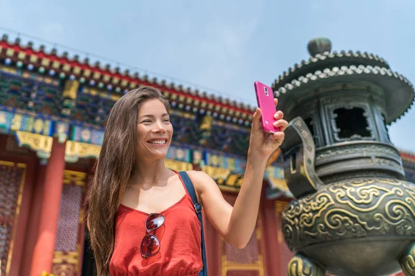 Chica tomando selfie teléfono en la atracción turística de China utilizando el teléfono inteligente en la antigua escultura de bronce templo en Beijing, China. Asia turismo de viajes. Personas durante las vacaciones — Foto de Stock