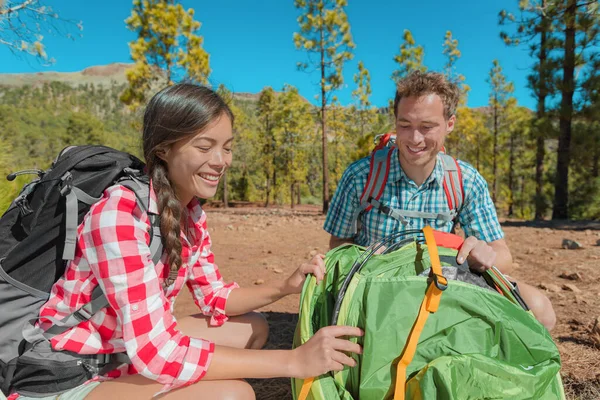 Zufriedene Camper, die ihr Zelt auf dem Campingplatz aufschlagen, um im Sommerurlaub auf Reisen zu zelten. asiatisch frau, kaukasier mann interracial gruppe von freunden — Stockfoto