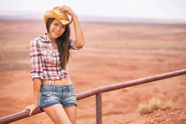 Cowgirl Frau lächelt in die Kamera mit Hut als Grußgeste glücklich auf dem Land Bauernhof Landschaft in Cowboy-Western-Hemd und Jeans. junge multirassische asiatische amerikanische Mädchen in der Wüste Landschaft — Stockfoto