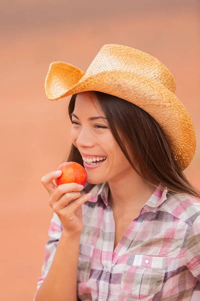 USA cowgirl eating peach nectarine fruit smiling wearing cowboy hat at outdoor country farm . Healthy food farmers market with beautiful young mixed race Caucasian Asian model — 图库照片